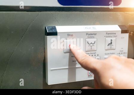 Close-up of a bidet control panel featuring various buttons, including a stop button. The image captures a hand pressing the control for personalized Stock Photo