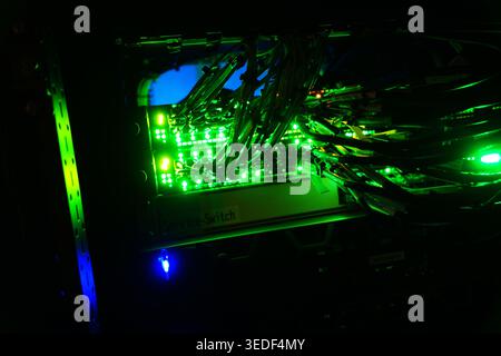 A close-up view of a network switch featuring glowing green lights, showcasing a complex arrangement of cables and electronics in a dim environment. Stock Photo