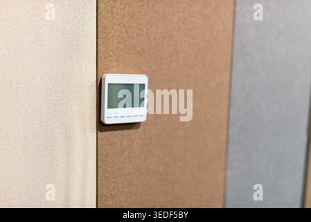 A sleek thermostat mounted on a multicolored wall, showcasing modern design and technology. Ideal for energy-efficient home temperature control. Stock Photo