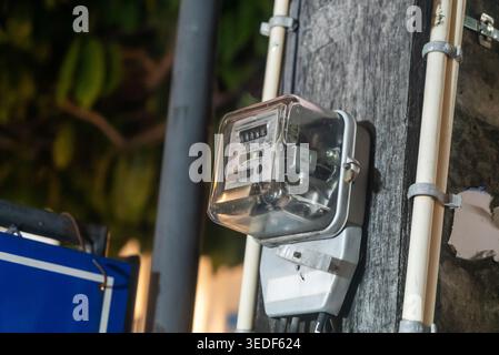 A close-up view of an energy meter mounted on a wooden pole in an urban setting at night, showcasing the technology for measuring electricity consumpt Stock Photo