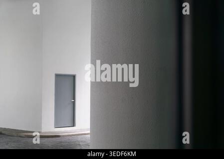 A minimalist architectural detail featuring a gray door against a white wall, framed by a column. The composition emphasizes simplicity and modern des Stock Photo