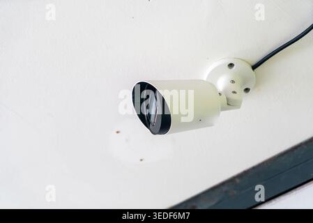 This image showcases a white security camera mounted on a ceiling, highlighting technology and surveillance for safety and monitoring in indoor spaces Stock Photo