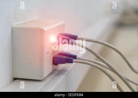 A close-up view of a network connection point featuring multiple Ethernet cables plugged in, with a glowing light indicator signaling active connectiv Stock Photo