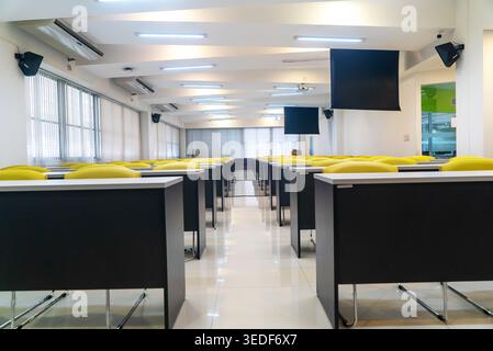 This image captures a modern empty classroom featuring yellow chairs and sleek desks. The spacious and bright interior promotes productivity and learn Stock Photo