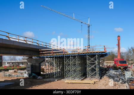 Large bridge construction project with tower crane, scaffolding and red mobile crane working on concrete overpass under clear blue sky Stock Photo