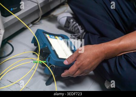 A technician works on network cables using a testing device, ensuring optimal connection and performance in a modern technological workspace. Stock Photo
