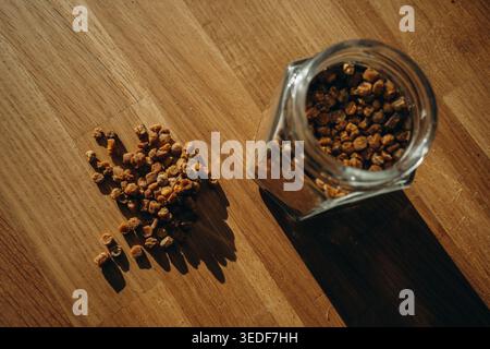 Glass jar of bee bread with granules spilled on a table. Natural beekeeping product, rich in vitamins, organic superfood and healthy nutrition concept Stock Photo