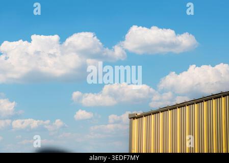 A striking image of a golden building against a vibrant blue sky filled with fluffy white clouds, showcasing the beauty of modern architecture in natu Stock Photo