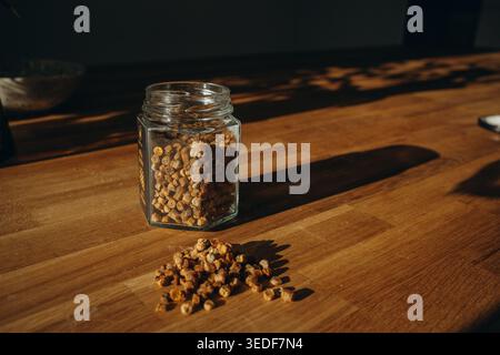 Glass jar of bee bread with granules spilled on a table. Natural beekeeping product, rich in vitamins, organic superfood and healthy nutrition concept Stock Photo