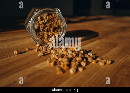 Glass jar of bee bread with granules spilled on a table. Natural beekeeping product, rich in vitamins, organic superfood and healthy nutrition concept Stock Photo