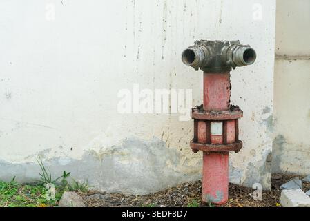 An aged fire hydrant stands against a weathered urban wall, showcasing its rusty metal surface and vibrant red color, symbolizing safety and emergency Stock Photo