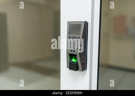 A modern biometric fingerprint scanner positioned near an entrance. The device features a keypad and a green signal indicating successful access. Stock Photo