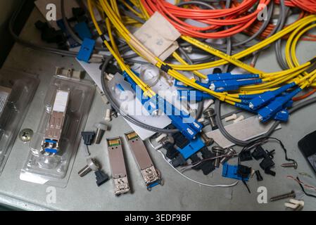 Closeup view of network equipment and colorful cables on a table, showcasing various connectors and tools in an unorganized arrangement, ideal for tec Stock Photo