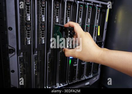 A hand holds a hard drive as it is being removed from a server rack unit. This image captures a moment of equipment handling in a modern data center e Stock Photo