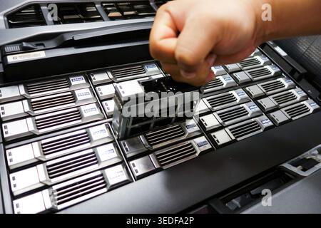 A hand is seen removing a hard drive from a server storage bay. This image captures the essential process of data management and equipment maintenance Stock Photo