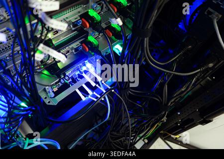 Detailed view of server room featuring network equipment and tangled cables with glowing lights. A showcase of modern data infrastructure. Stock Photo