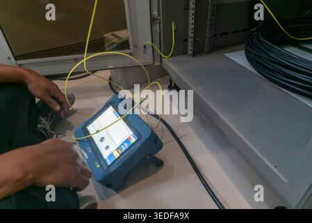 A technician uses a fiber optic measurement device to test and analyze network performance in a modern workspace. The device aids in cable installatio Stock Photo