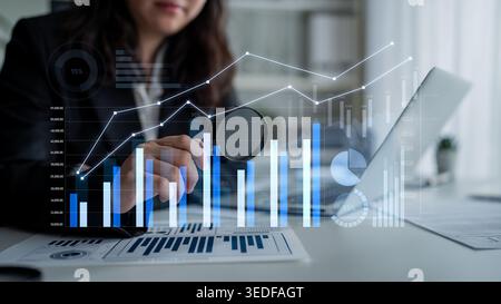 A businesswoman examines financial data on her desk using a magnifying glass, showcasing interactive graphs and charts that represent growth and Stock Photo