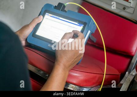 A person interacts with a tablet device while seated on a red chair, showcasing modern technology in a transport setting, reflecting user engagement a Stock Photo
