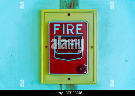 Bright red fire alarm button mounted on a yellow wall, designed for emergency alerts. This safety device ensures quick response to fire hazards. Stock Photo