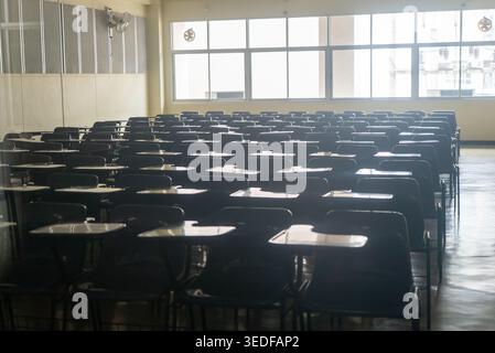A spacious empty classroom showcasing rows of desks and chairs, illuminated by natural light from large windows, highlighting an inviting learning env Stock Photo