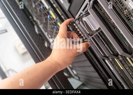A close-up view of a hand installing a data storage device into a server rack, showcasing technology and infrastructure in a professional IT environme Stock Photo