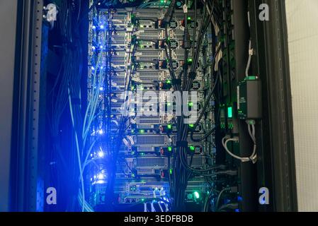 Detailed view of a server rack filled with hardware and illuminated by blue LED lights, showcasing the complexity of data processing and connectivity Stock Photo