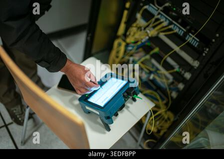 A technician uses a testing device to analyze network performance in a server room. The image captures the essential tools and technology for diagnosi Stock Photo