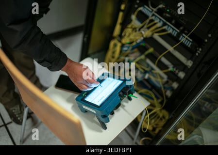 A technician operates advanced equipment to analyze network connections in a server room. Cables and devices surround the workspace, highlighting tech Stock Photo
