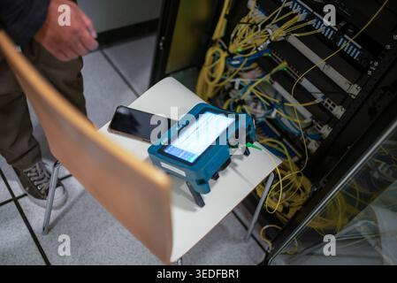 A close-up view of data cable testing equipment in a modern office setting, highlighting its connection to a network, smartphone, and workstation elem Stock Photo