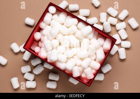 Gift box with packing peanuts on brown background, flat lay Stock Photo
