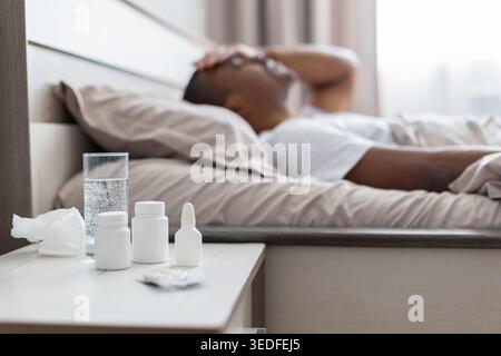 African american man lying sick in bed with medicines on bedside table Stock Photo