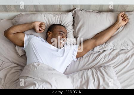 African american man stretching in bed after waking up smiling Stock Photo