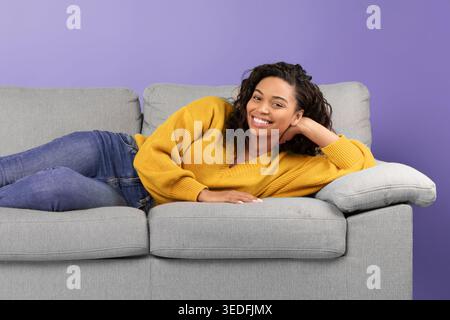 Young Woman Relaxing on Couch in Living Room With Purple Wall in Background Stock Photo