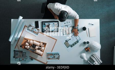 Top view of business man using tablet plan house design while sitting at meeting table with blueprint and equipment scatter around. Aerial view of Stock Photo