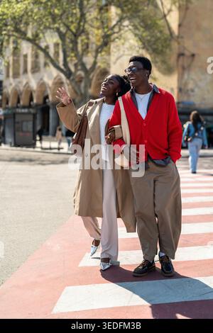 Carefree african american friends man and woman walk along crosswalk laughing and talking. Stock Photo