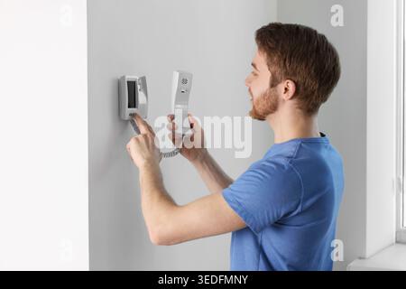 Man with handset pressing button on intercom panel indoors Stock Photo