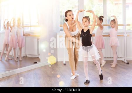In studio, mentor corrects girls arm and leg, teaches correct dynamics and execution of movements Stock Photo