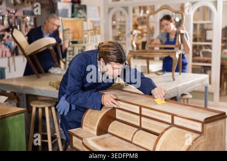 Middle-aged male polishes tabletop of old chest of drawers with rounded drawers with soft cloth Stock Photo