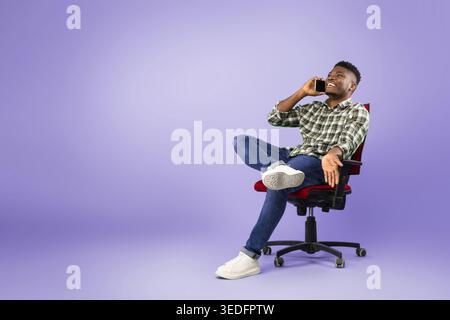 Man Talks on Phone While Sitting in Office Chair Against Purple Background Stock Photo