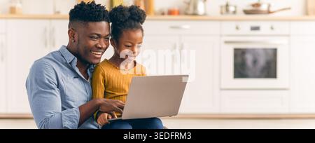 Father and Daughter Share Time Together Using a Laptop in a Kitchen Setting Stock Photo