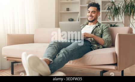 Man Using Laptop While Sitting on Sofa in Cozy Living Room During Daylight Hours Stock Photo