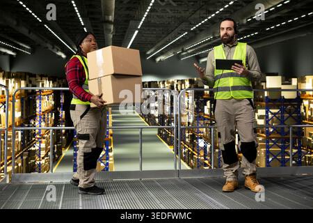 Logistics operator, assisting customers, order fulfillment, delivery tracking, wearing headset and safety vest. Man checking parcel status via airway bills on tracking software, supply chain. Stock Photo