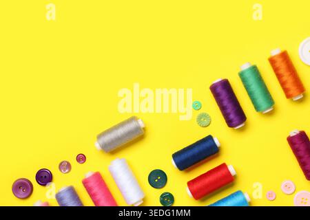 Composition with many different thread spools and buttons on yellow background Stock Photo