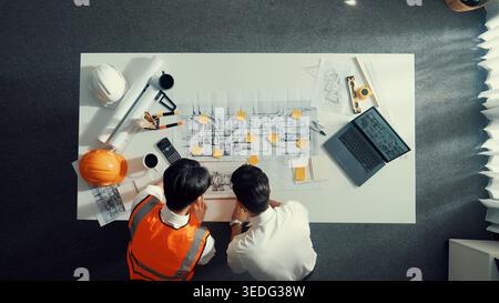 Top view of manager writing idea while engineer holding plan. Group of diverse people working together and planning building construction at meeting Stock Photo