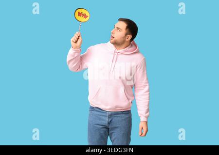 Shocked young man holding speech bubble with word WOW on blue background Stock Photo