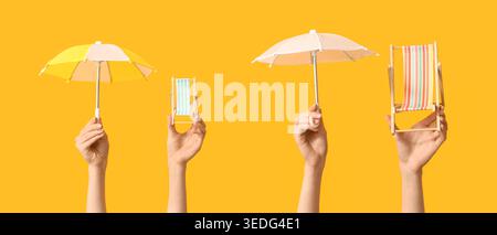 Hands holding mini deck chairs with umbrellas on yellow background Stock Photo