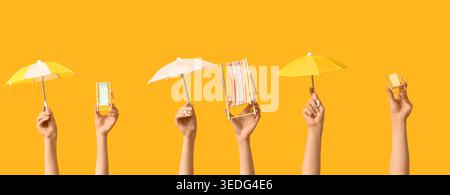 Hands holding mini deck chairs with umbrellas on yellow background Stock Photo