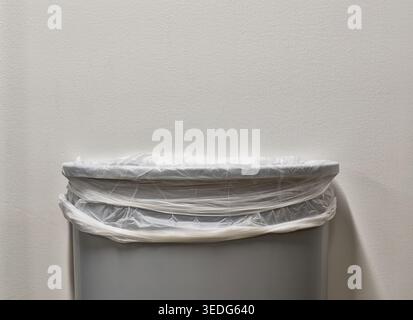 Gray trashcan partial with trash bin liner by white plain wall with copy space. Stock Photo