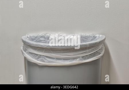 Gray trashcan partial with trash bin liner by white plain wall with copy space. Stock Photo